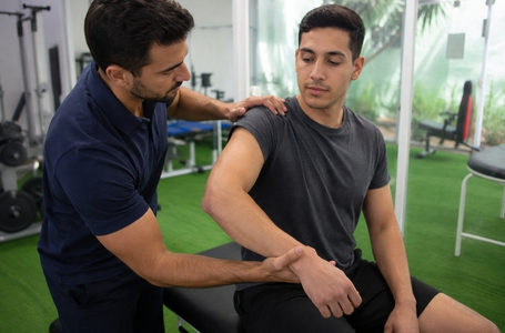 Fisioterapeuta avaliando pescoço, ombro e braço de paciente com sintomas de síndrome do desfiladeiro torácico em clínica moderna de fisioterapia.