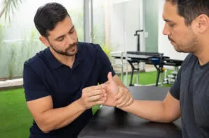 Fisioterapeuta avaliando a base do polegar e a força de pinça de paciente com suspeita de rizartrose em clínica moderna.